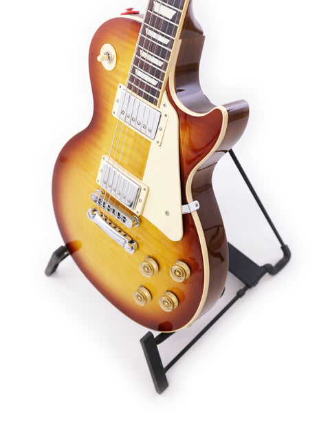 Elegant Gibson Les Paul Traditional guitar resting on a stand, highlighted by a minimalist white background for a classic look.