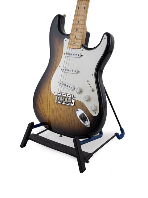 Fender Custom Shop 1954 Strat guitar on a stand, set against a sleek black background, showcasing its elegant design.