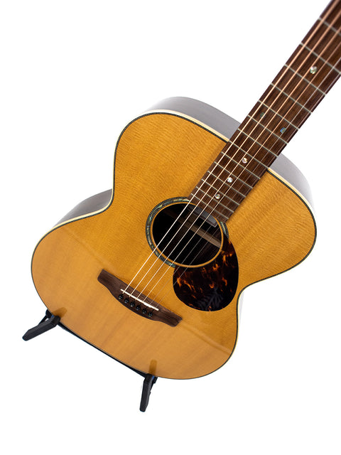 Gerard Gilet 000 14 Fret acoustic guitar displayed on a stand, contrasting with a bright white backdrop.