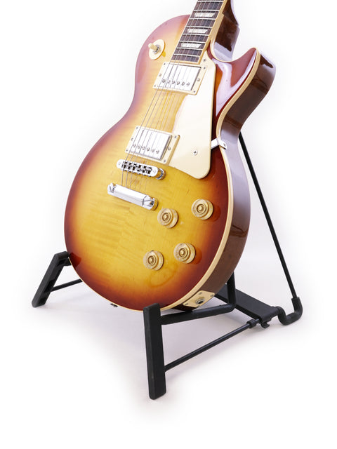 Gibson Les Paul Traditional guitar displayed on a stand, featuring a striking white background that highlights its beauty.