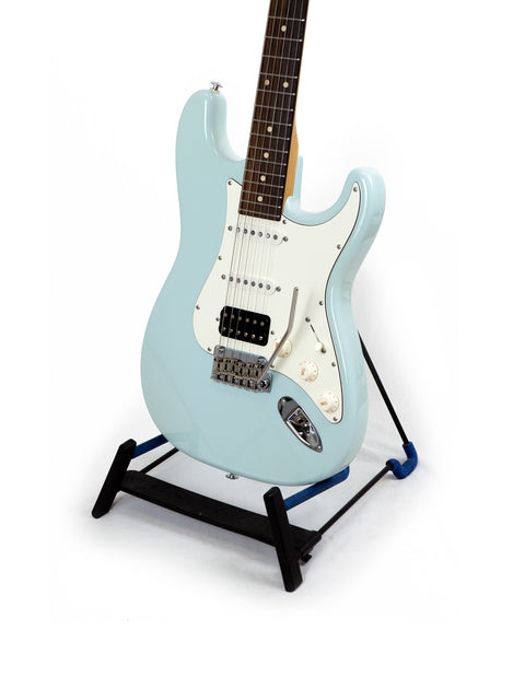 Suhr Classic Pro electric guitar in blue, elegantly positioned on a black base stand, emphasizing its modern style.