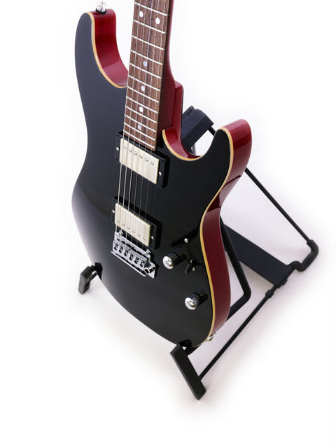 Suhr Pete Thorn Signature electric guitar in black with a red pickguard, elegantly positioned on a stand.
