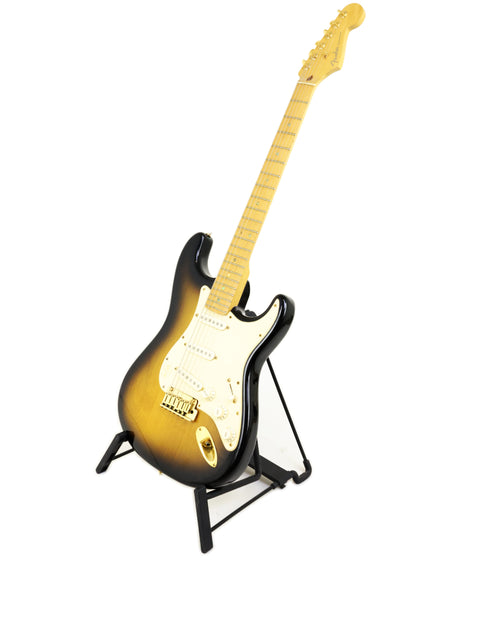 Sunburst electric guitar with a maple neck on a stand, isolated on a white background.
