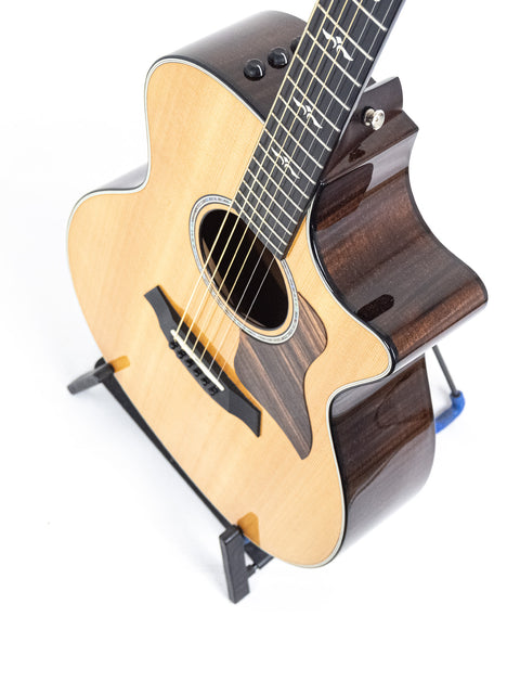 Taylor 614ce guitar displayed on a stand, set against a bright white background, highlighting its beautiful features.