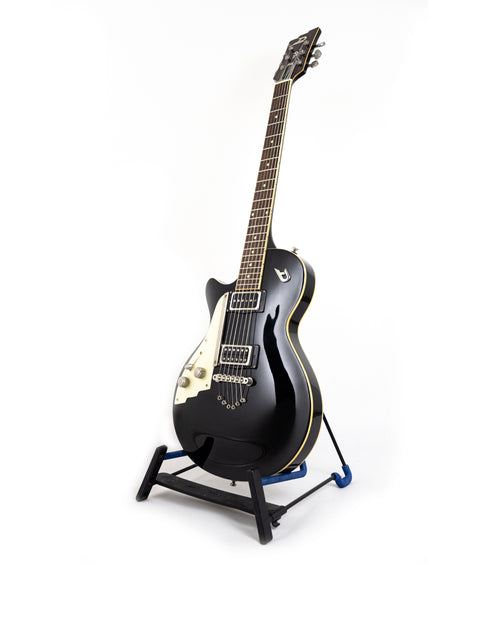 The Duesenberg 49er Solid Body guitar, black and elegant, displayed on a stand with a bright white backdrop for contrast.
