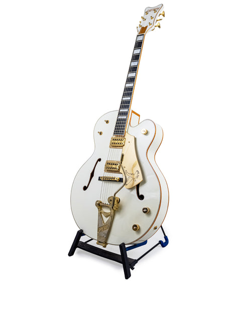 The Gretsch G7593 White Falcon, a white guitar with gold hardware, stands proudly on a display stand, highlighting its beauty.