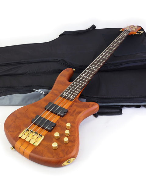 The image features a Schecter Stiletto Studio 4 bass guitar, neatly placed in a case with a bag, highlighting its stylish appearance.