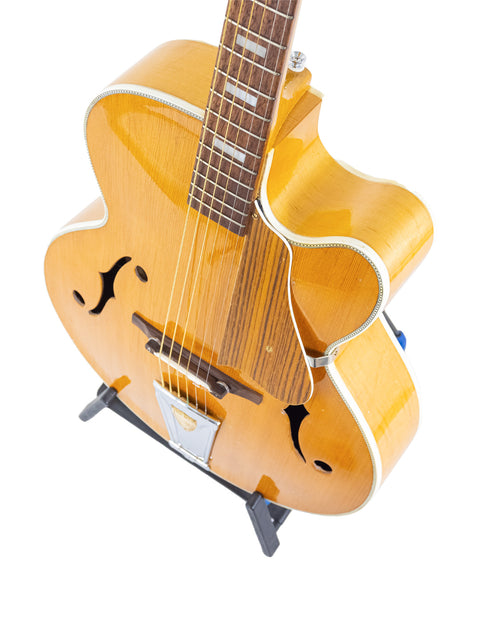 Vintage 1970s yellow Sutton Archtop guitar on a stand, set against a bright white backdrop.