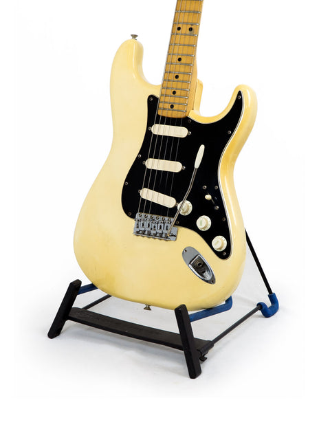 Vintage 1976 Fender Stratocaster guitar in white, elegantly positioned on a stand with a black base.