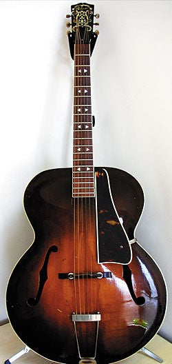 Vintage Gibson L 7 Special guitar from the 1940s resting on a stand, set against a stark white background for emphasis.