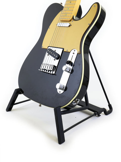 striking black and gold Fender American Deluxe Telecaster guitar resting on a stand, showcasing its sleek design.