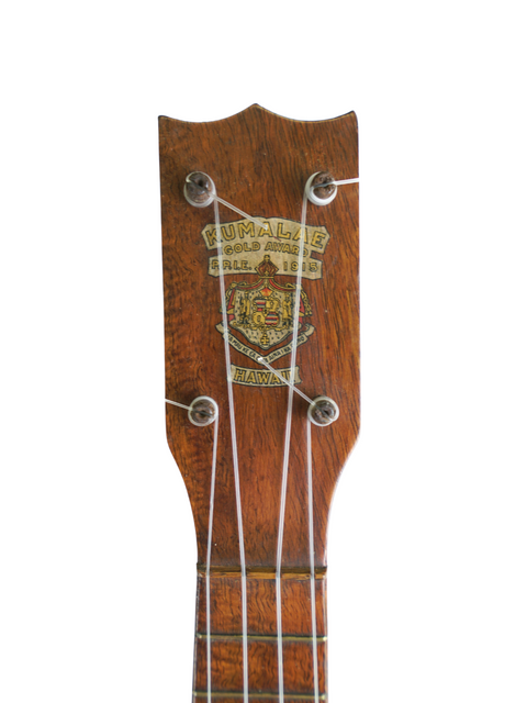 1930s Kumalae Model D ukulele with a wooden body and a gold and silver headstock, representing vintage Hawaiian craftsmanship.