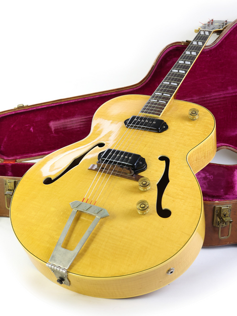 1952 vintage Gibson ES-300 guitar in yellow, elegantly placed in its case on a pristine white surface.
