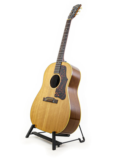 1956 Gibson J-50 guitar elegantly positioned on a stand, contrasting with a pristine white background.