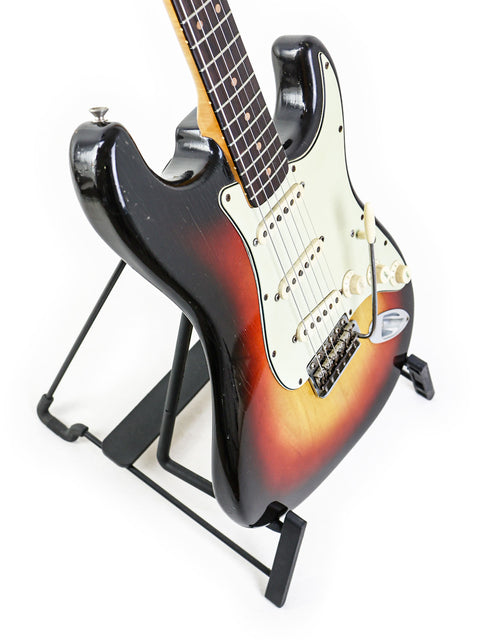1963 Fender L-Series Stratocaster resting on a stand, highlighted by a black background.