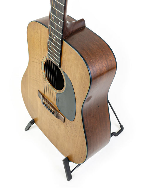 1974 Martin D-18 guitar elegantly positioned on a stand with a plain white backdrop.