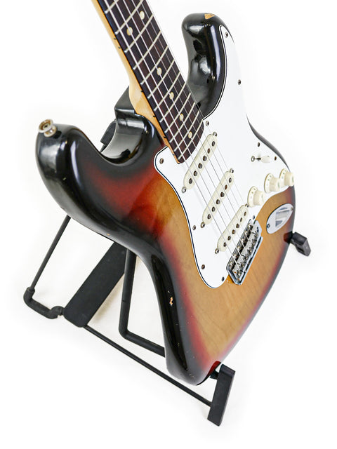 1974 vintage Fender Stratocaster guitar positioned on a stand, set against a white background.