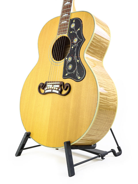 1999 Gibson SJ-200 guitar resting on a stand, set against a plain white backdrop.