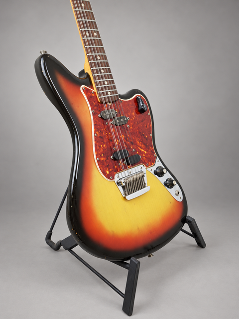 A stunning vintage Fender Electric XII guitar with a sunburst finish, proudly standing on its display stand.