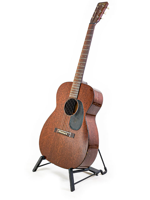 A 1954 Martin 00-17 guitar resting on a stand, set against a stark white background.
