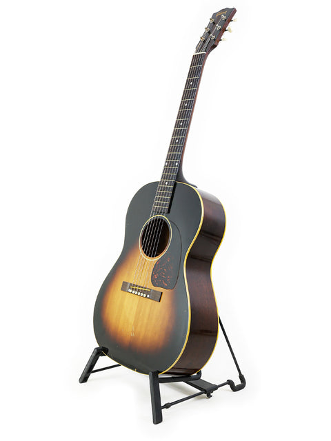 A 1954 Vintage Gibson LG-1 guitar displayed on a stand with a simple white background, highlighting its timeless appeal.