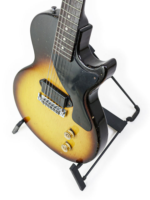 A 1958 Gibson Les Paul Jr TV Yellow Refin guitar showcased on a stand, featuring a stark white background.
