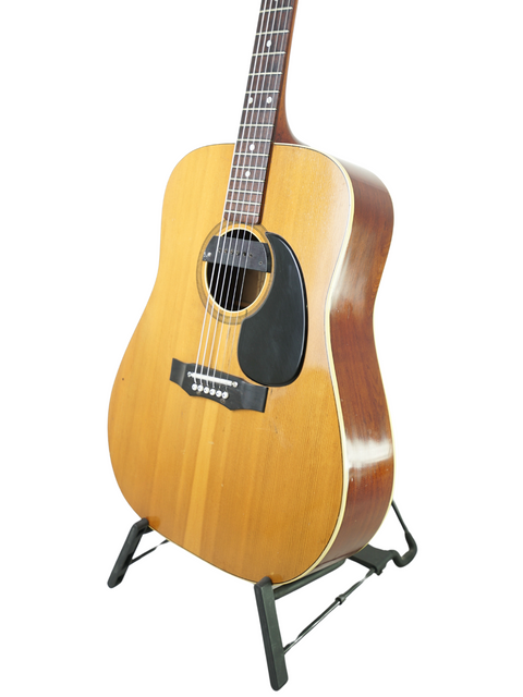 A 1972 Maton FG100 guitar showcased on a stand with a simple white background.