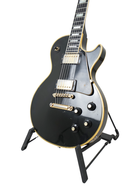 A 1973 Gibson Les Paul Custom Black Beauty, a black electric guitar, showcased on a stand.
