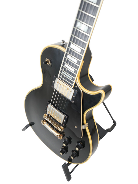 A 1973 Gibson Les Paul Custom Black Beauty electric guitar showcasing a black body and elegant gold pick guard.