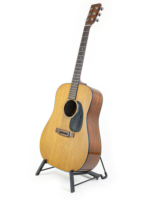 A 1974 Martin D-18 guitar on a stand, showcasing its vintage charm against a bright white background.