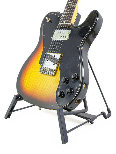 A 1977 Fender Telecaster Custom guitar elegantly positioned on a stand with a dark black backdrop.