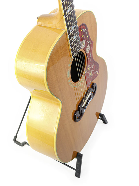 A 1984 Gibson SJ-200 guitar elegantly positioned on a stand with a white backdrop.