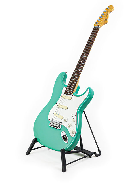 A 1989 green Fender Strat Plus Deluxe guitar elegantly positioned on a stand with a white backdrop.