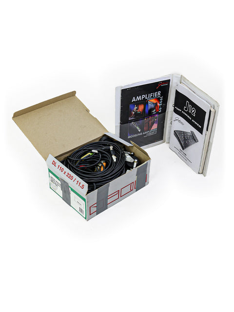 A 1998 Johnson Millennium Stereo 250 Modeling Amplifier in a box, with a computer and a connecting cable visible.