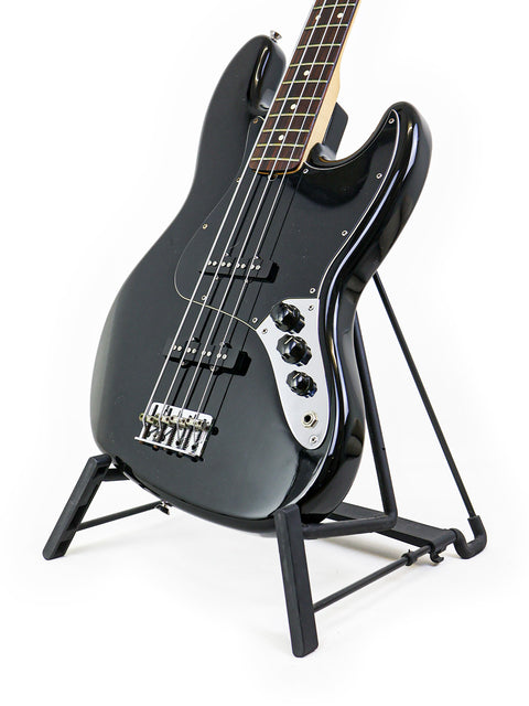 A 2005 black Fender Jazz Bass guitar on a stand, contrasted by a simple white background, emphasizing its classic look.