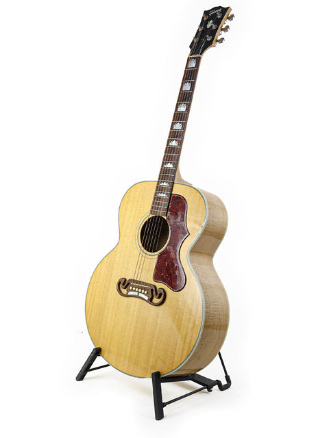 A 2008 Gibson SJ-150 guitar resting on a stand, set against a bright white backdrop.
