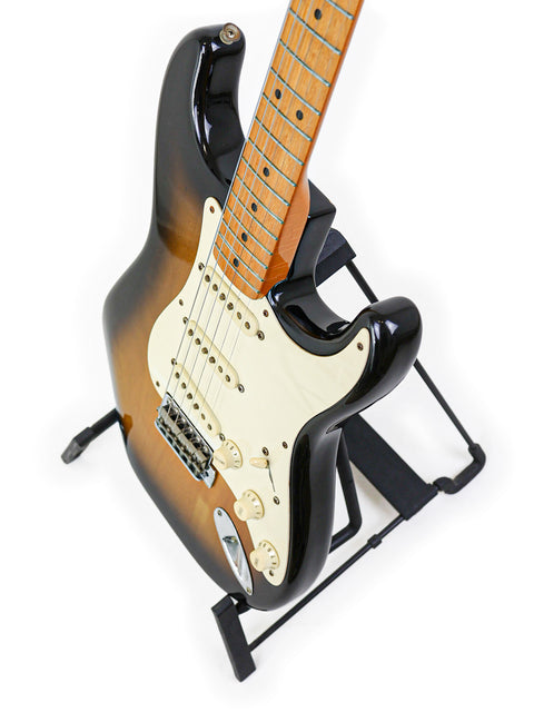 A Fender AVRI ‘57 Stratocaster from 1982 on a stand, beautifully contrasted against a solid black background.