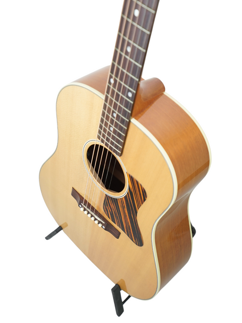 A Gibson J-35 guitar from 2013 stands proudly on a stand, set against a minimalist white backdrop for a striking look.