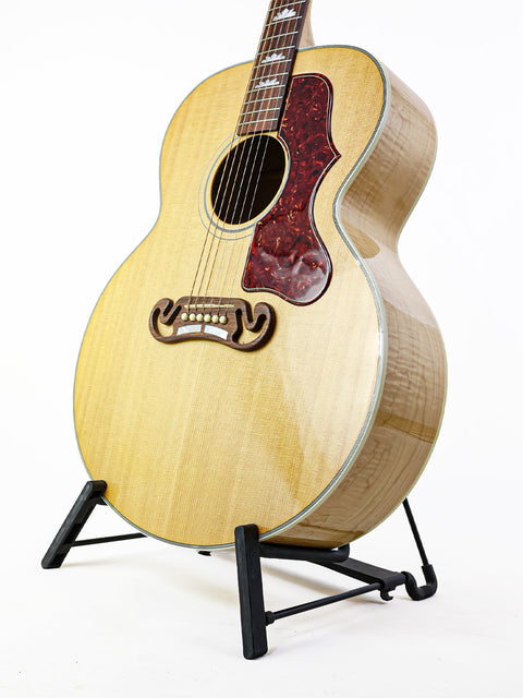 A Gibson SJ-150 guitar from 2008 displayed on a stand against a clean white background.