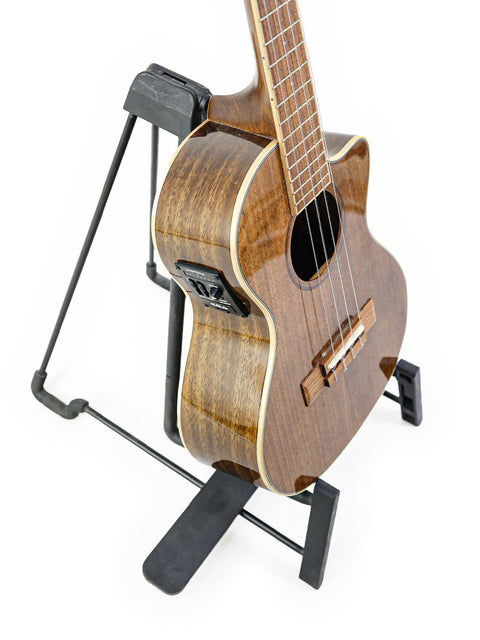 A beautifully crafted Kala KA-KTGE-C Hawaiian Koa Tenor Cutaway Ukulele on a stand, featuring its exquisite koa wood texture.