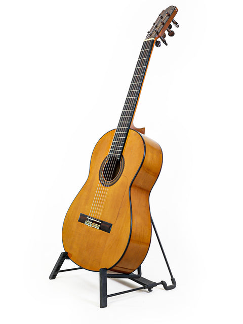 A beautifully crafted guitar displayed on a stand with a white backdrop, highlighting its features and Spanish origin from 1973.