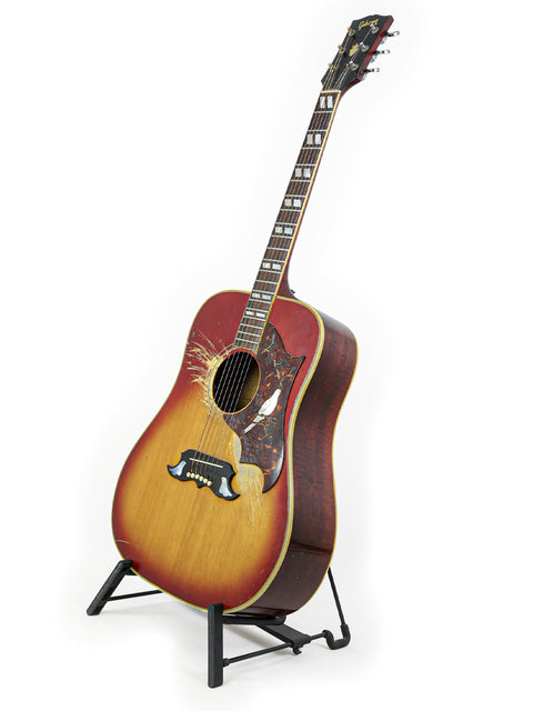 A bird sits atop a 1968 Vintage Gibson Dove guitar, elegantly displayed on a stand
