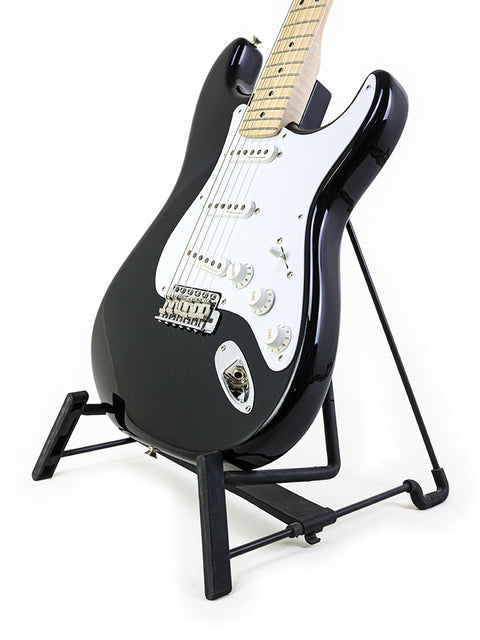 A black Fender Eric Clapton "Blackie" Stratocaster guitar on a stand against a clean white background.
