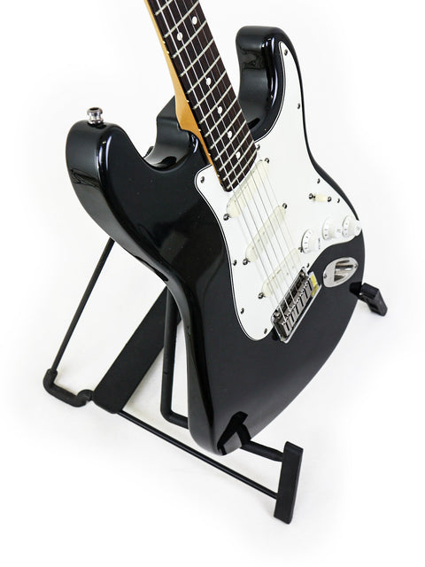 A black Fender Strat Plus guitar, model year 1991, showcased on a stand with a stark white background.