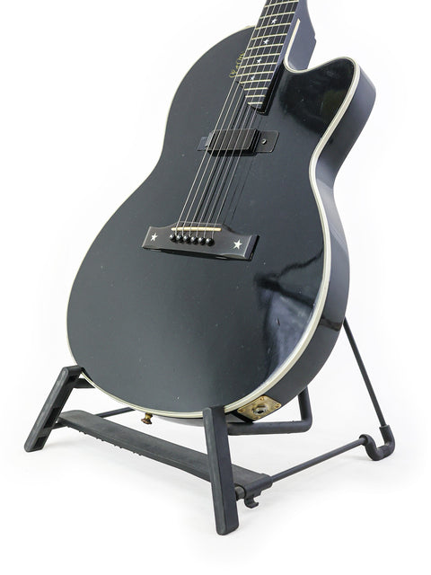 A black Gibson Chet Atkins SST guitar displayed on a stand, set against a stark white background, highlighting its features.