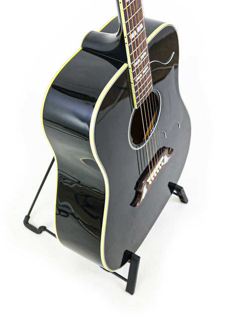 A black Gibson Custom Shop Elvis Dove acoustic guitar displayed on a stand with a white backdrop.