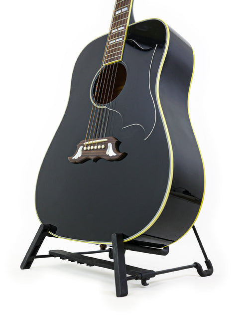 A black acoustic guitar on a stand, showcasing the 2023 Gibson Custom Shop Elvis Dove from the USA.