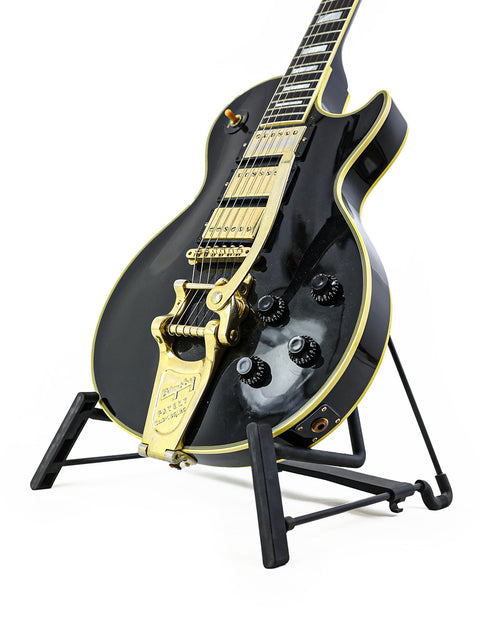 A black and gold 2004 Gibson Custom Shop 1957 Les Paul Custom B3 guitar resting on a stand, highlighting its classic style.