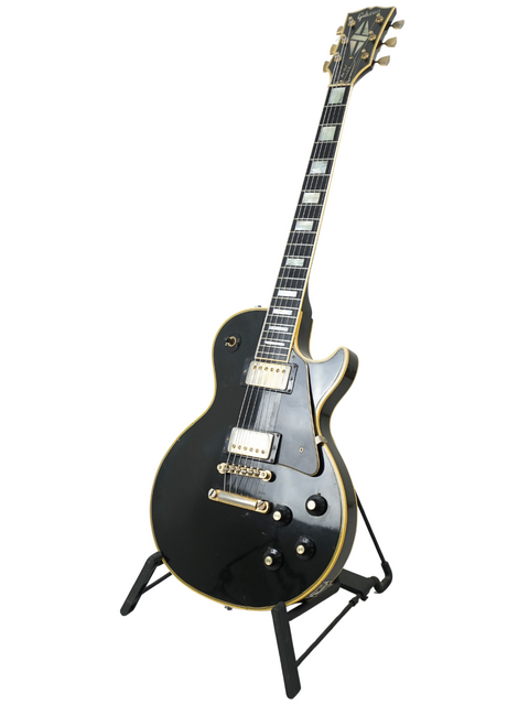 A black electric guitar, the 1973 Gibson Les Paul Custom Black Beauty, elegantly positioned on a stand for display.