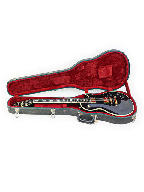 A black guitar, the 1991 Gibson Les Paul Custom, resting in a case on a stark white background.